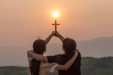 Silhouette two girl together hug with holding christian cross for worshipping God on the mountain...