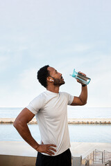 Vertical portrait of Black male runner taking a break to drink water. Copy space..