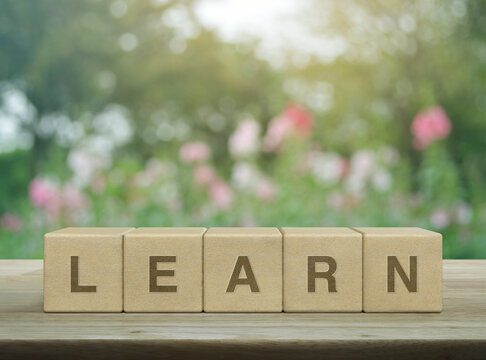 Learn letter on wood block cubes on wooden table over blur pink flower and tree in garden, Business, education and learning concept