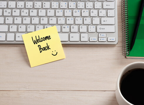 Welcome back message handwritten on a sticky note paper on the office desk.