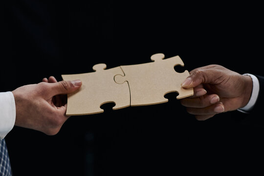 See the big picture. Close-up of an unidentified business man holding two puzzle pieces together.