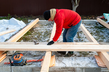 A man in a red jacket is engaged in construction using wooden planks - 755388770