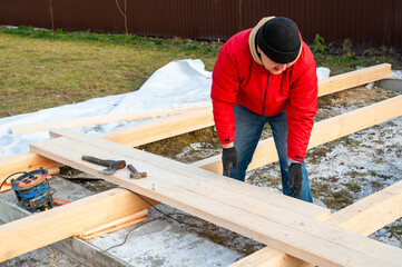 A man in a red jacket is engaged in construction using wooden planks - 755388966