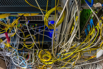 A mess of cables and wires on the back of the devices. Disorganized and careless wiring connecting computer servers in data center room.