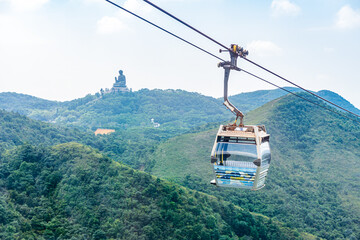 Overhead cable car riding through the mountain with Tian Tan Buddha statue on the far peak. It is one of transportations to the tourist attractions located at Ngong Ping, Lantau Island, in Hong Kong.