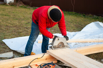 A man in a red jacket is engaged in construction using wooden planks - 755391167