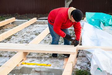 A man in a red jacket is engaged in construction using wooden planks - 755391741