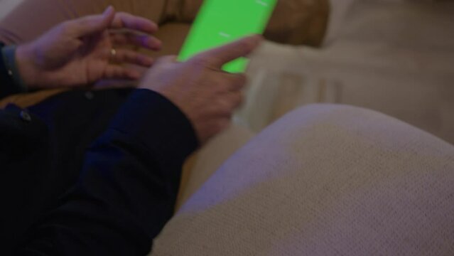 Man Sitting on his Sofa in conversation, receives notification on his smartphone, green screen