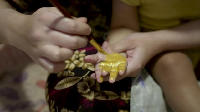 A person paints a toddler's hand with shimmering gold paint, fostering creativity and bonding through artful experimentation and fun moments.