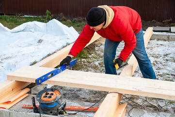 A man in a red jacket is engaged in construction using wooden planks. Measures level