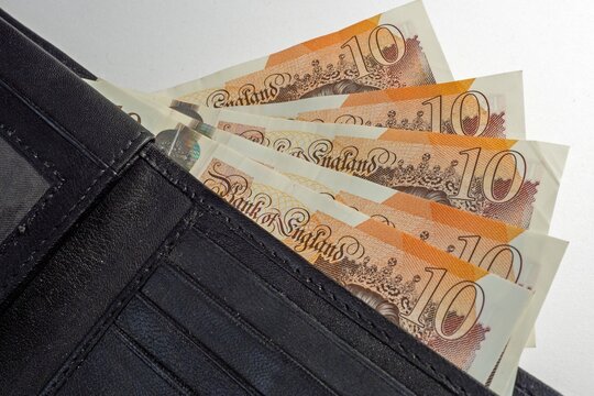 Close-up photograph of five british ten pound bank notes protruding from a wallet with each note showing the number 10