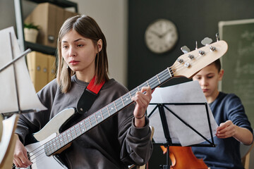 Selective focus shot of Caucasian teen girl practicing bass guitar during music lesson at school © AnnaStills