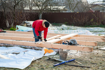 A man in a red jacket is engaged in construction using wooden planks - 755397507