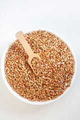 De hulled buckwheat with scoop in a white bowl, isolated on white