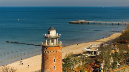 A sunny day in February at Kołobrzeg port, Poland. The image captures a red brick lighthouse, tourists strolling on the sandy beach, and a distant pier, with calm sea waters. - obrazy, fototapety, plakaty