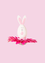 Easter bunny in the shape of egg on a natural pink daisy flower levitate on pastel pink background....