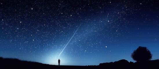 A person is standing in front of a tree, looking up at the sky