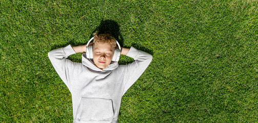 A boy relaxing on grass, listening to music - 755407578