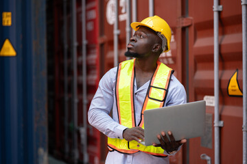 African American logistic engineer man worker or foreman holding notebook computer with container background at container site	