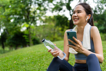 Asian young women drink water from a plastic bottle after exercises or sports. Asian woman running in garden. Beautiful fitness athlete woman drinking pure water after workout exercise on morning