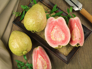 Fresh pink guava fruit, pieces and leaves isolated on wooden background.