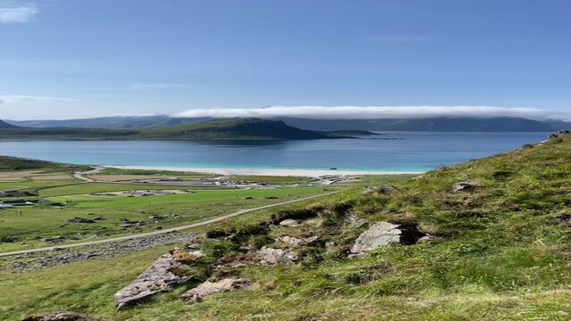 View of Hauklandstranda from the Mannen mountain top, Lofoten, Norway, sunny summer day, white sandy beach, blue sea. Low clouds on distant mountain tops, green vivid nature.