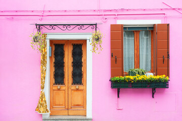 Pink painted facade of the house, door and window with flowers. Burano, Italy.