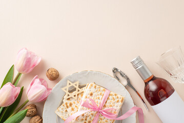 Top view picture of a Passover seder plate with matzah in a ribbon, a red wine bottle, a glass, nuts and nutcracker, star of David, and fresh tulips, on a pastel beige surface