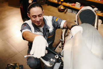 Smiling repairman checking leverage of motorcycle