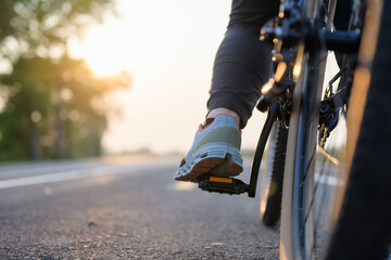 Closeup foot of the bicycle rider on the pedal while riding along the asphalt road in countryside at sunset