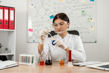 Woman scientist chemist  mixing liquid in laboratory glass with pipette,