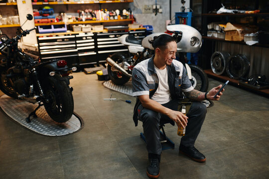 Mechanic drinking beer and checking social media after work