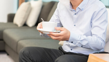 Fototapeta na wymiar Hands of male holding a cup of tea, sitting on the sofa. A pause in the work, a cup of coffee.