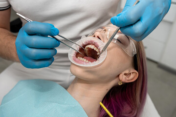 male dentist and a female assistant operate on a young smiling woman in a dental clinic.