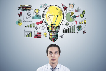 Portrait of thoughtful young businessman with creative business sketch with huge light bulb and...