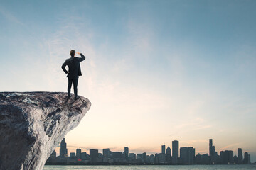 Fototapeta na wymiar Businessman standing on cliff edge on bright blue sky with mock up place background. Future, success and tomorrow concept.