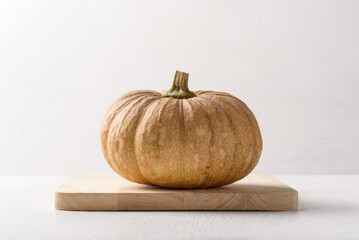 Local pumpkins are placed on a light brown wooden plank on a white background. Organic ingredients for healthy cooking