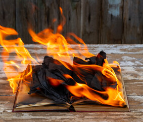 An open book burning in a fire on an old wooden table in close-up