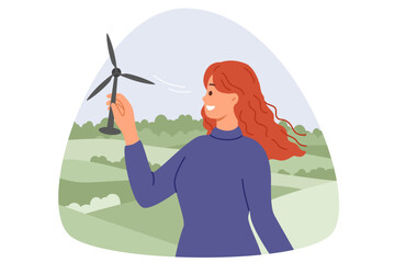 Wind turbine in hands of woman with smile standing in nature, and developing alternative and regenerative energy. Girl installs miniature wind turbine to generate electricity from renewable sources.