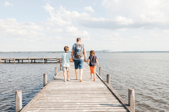 Father walking with sons on wooden pier at lake