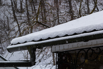 Snow on the roof of a red, brown metal tile of a European house