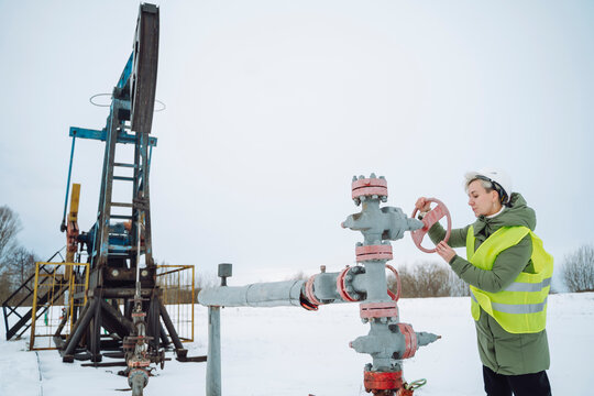 Engineer operating wellhead near drilling tower at oil field in winter