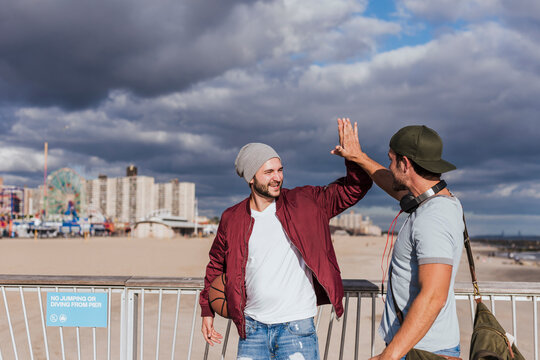 Happy friends giving high-five walking near railing at beach