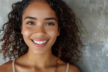 A woman with curly hair is smiling and looking at the camera. She has a bright, happy expression on her face