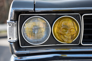 Detail of the round yellow headlight in the shape of a skull on a classic American style car