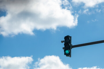 Green traffic light on blue cloudy sky background