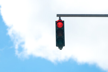 Red traffic light on blue cloudy sky background
