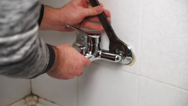 Plumber fixing repairing leaky shower Bathtub water tap faucet by wrench tool close up. Budget friendly replacement of plumbing fixtures by non professional in old bathroom with mold on wall tiles