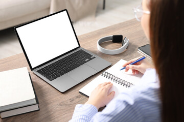 E-learning. Woman taking notes during online lesson at table indoors, closeup