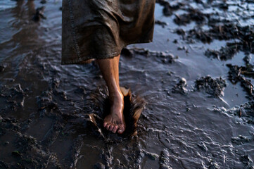 Bare feet of a dirty woman wading through mud puddles